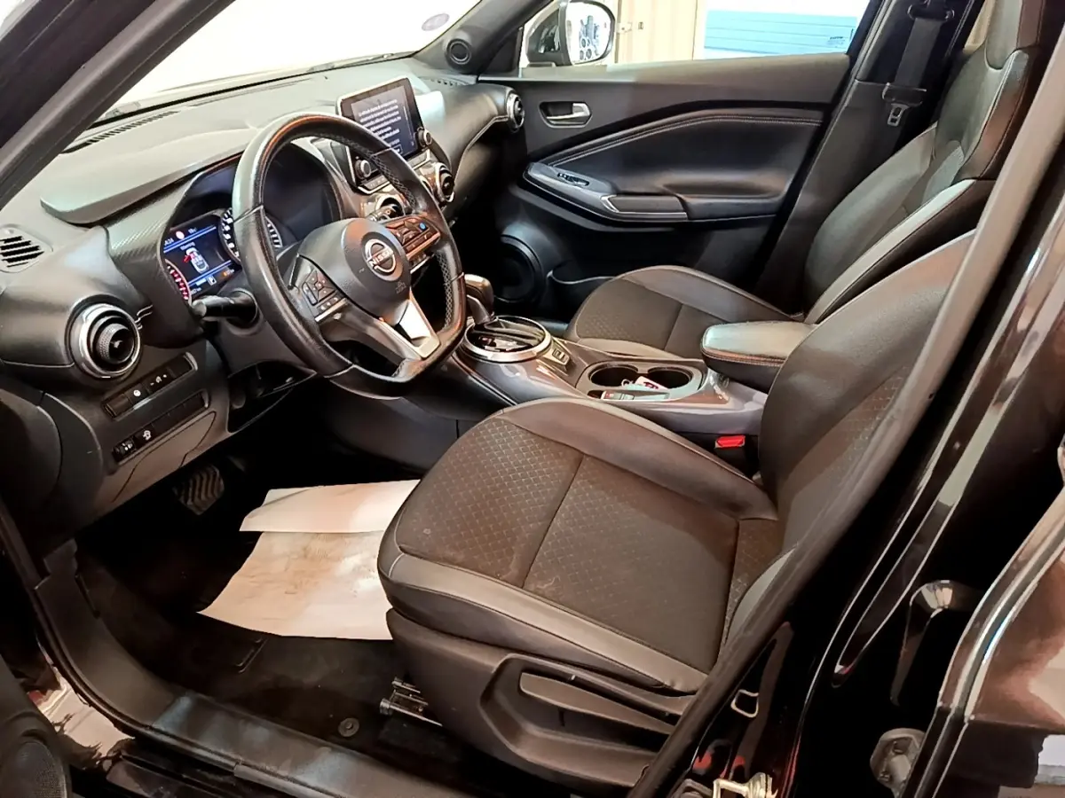 Vue intérieure côté conducteur du Nissan Juke noir 2022, montrant sièges, volant multifonctions et écran tactile central.