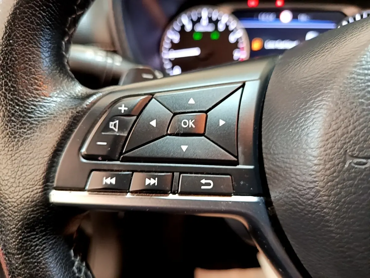 Gros plan sur les commandes gauche du volant noir du Nissan Juke 2022 avec tableau de bord lumineux en arrière-plan.