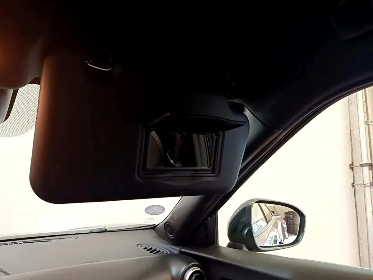 Intérieur du Nissan Juke 2022 noir, vue côté passager avec pare-soleil baissé et rétroviseur extérieur visible.