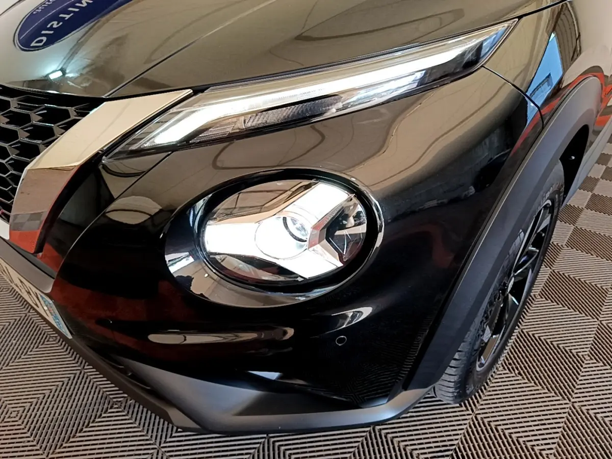 Gros plan sur l'avant droit noir brillant du Nissan Juke 2022, mettant en valeur son phare rond et son optique LED étirée.
