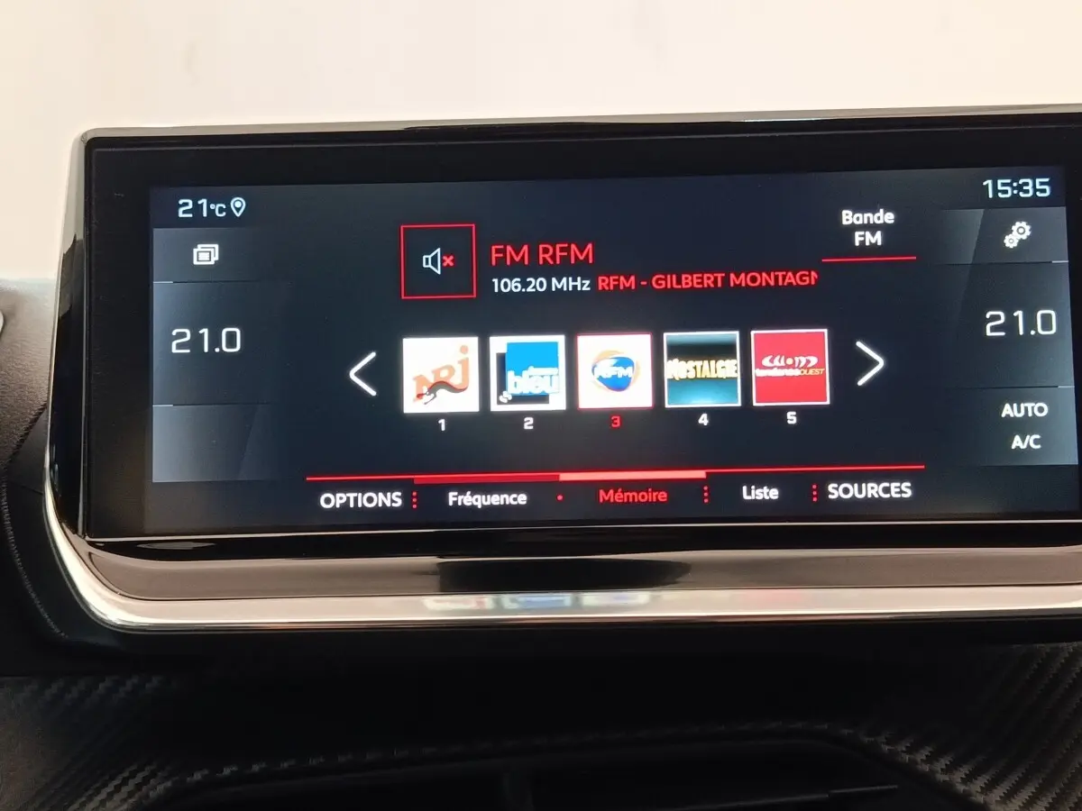 Écran tactile central 10 pouces du tableau de bord de la Peugeot 208 blanche, affichant la radio FM.