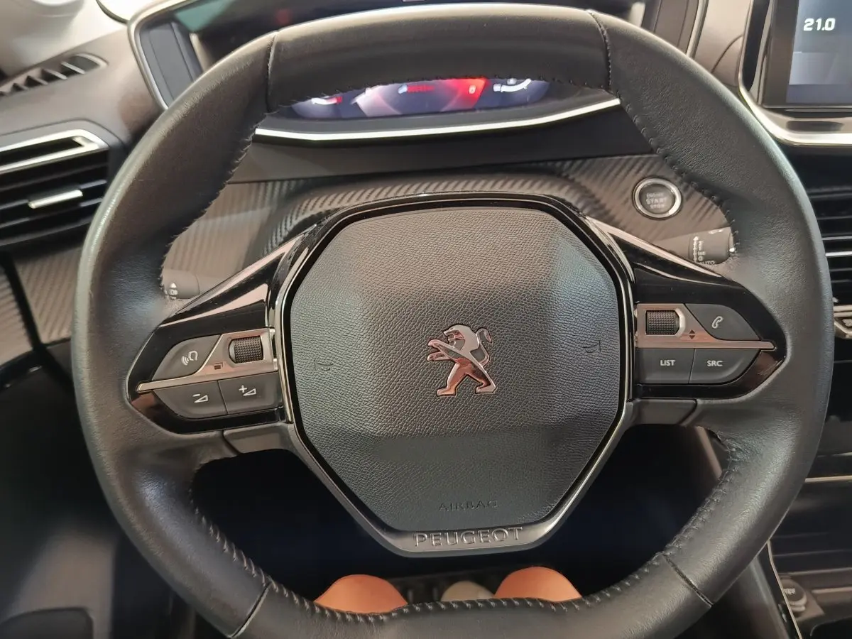 Vue rapprochée du volant cuir noir de la Peugeot 208 blanc, avec commandes intégrées et bouton démarrage visible.