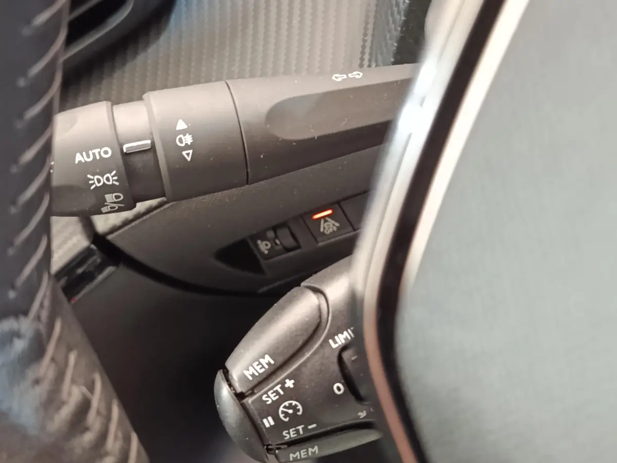 Gros plan sur commandes au volant et commodo d’éclairage d’une Peugeot 208 blanche, version PureTech 100 S&S Allure Business.
