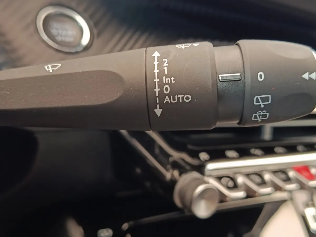 Gros plan sur la commande des essuie-glaces noire dans l'habitacle d'une Peugeot 208 blanche, avec bouton démarrage visible.