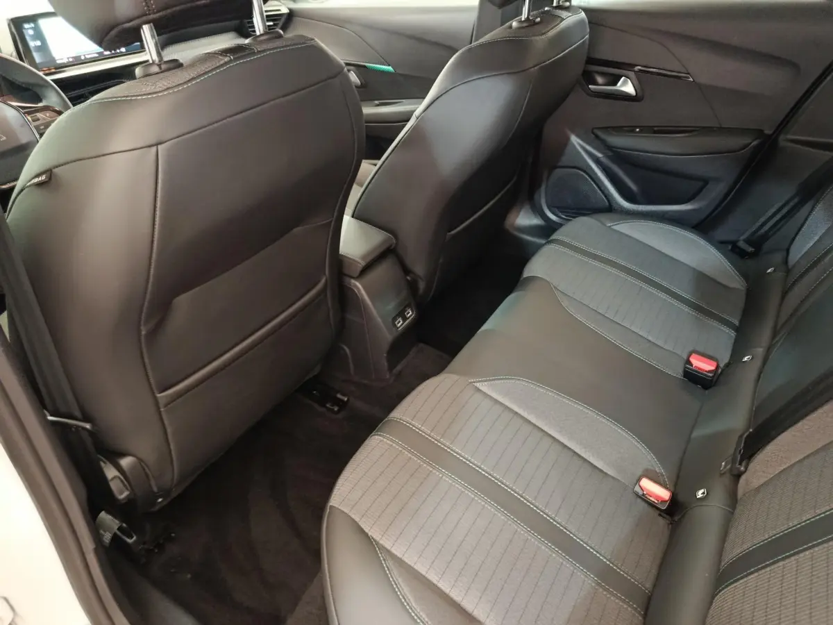 Vue intérieure arrière côté droit de la Peugeot 208 blanche, montrant la banquette et les sièges avant en cuir noir.