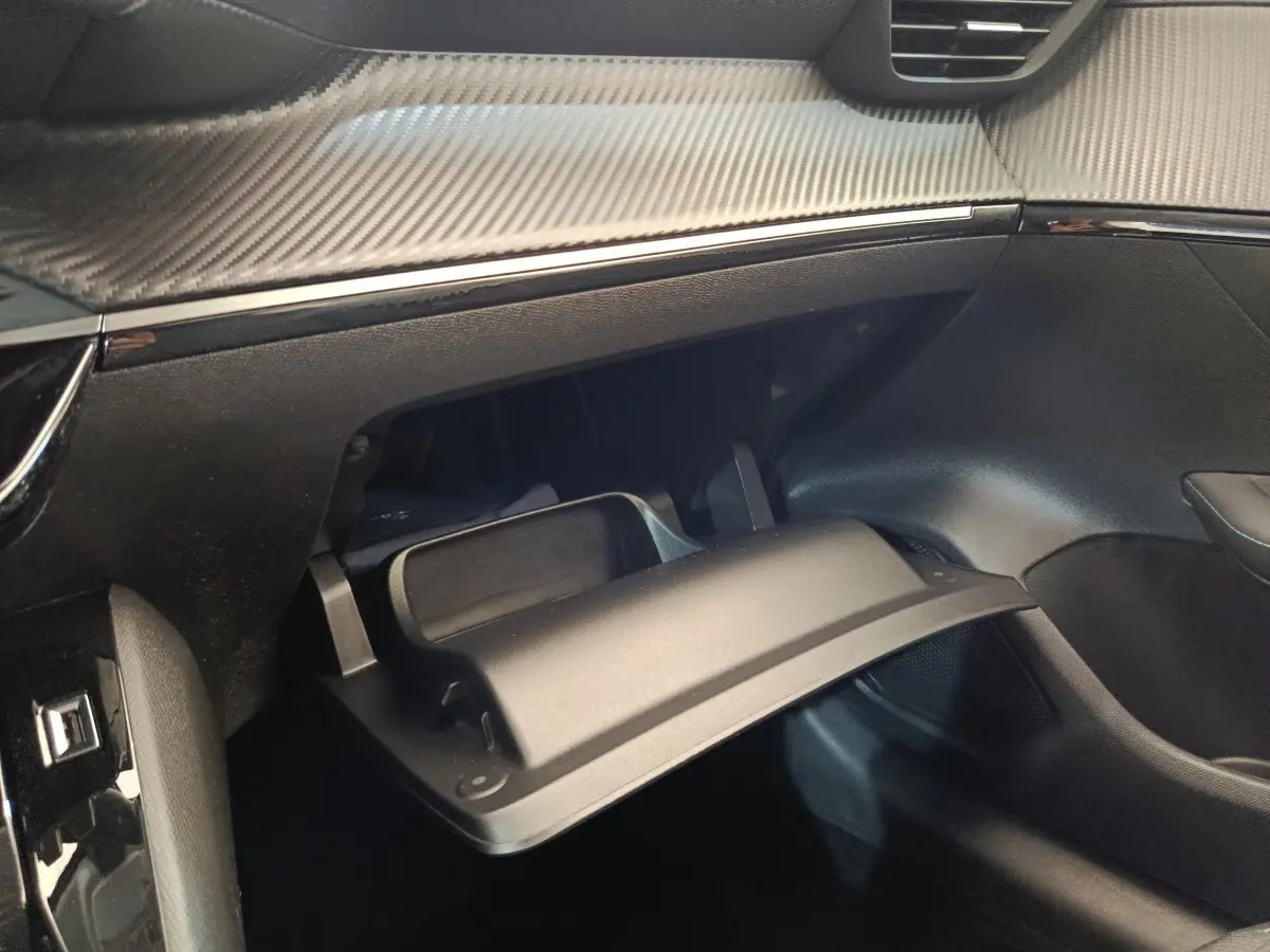 Vue intérieure côté passager du coffre à gants ouvert avec tableau de bord noir et finition effet carbone sur Peugeot 208 blanc.