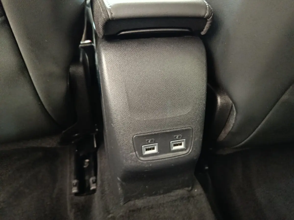 Vue rapprochée des ports USB arrière noirs situés entre les sièges avant d'une Peugeot 208 blanche.
