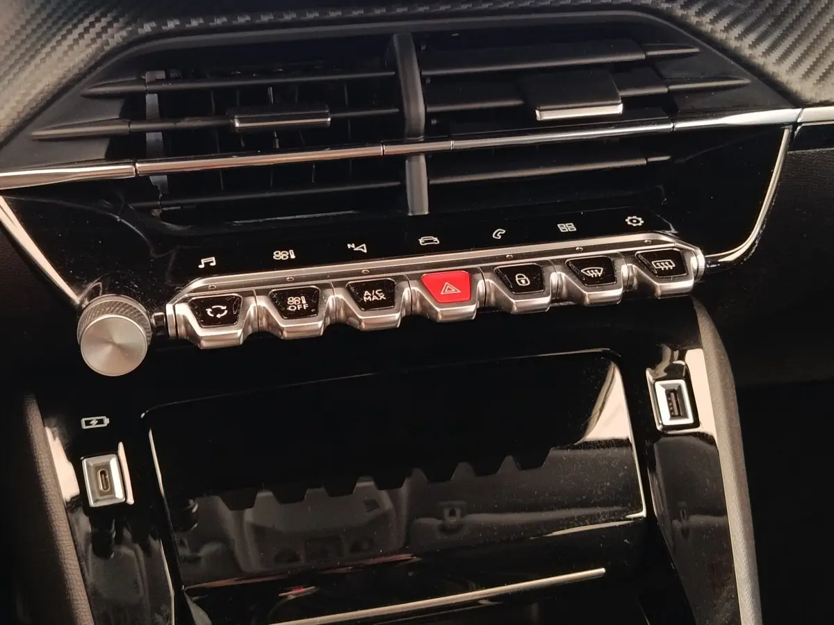 Vue rapprochée de la console centrale noire brillante de la Peugeot 208 PureTech 100 avec boutons de commande et ports USB.