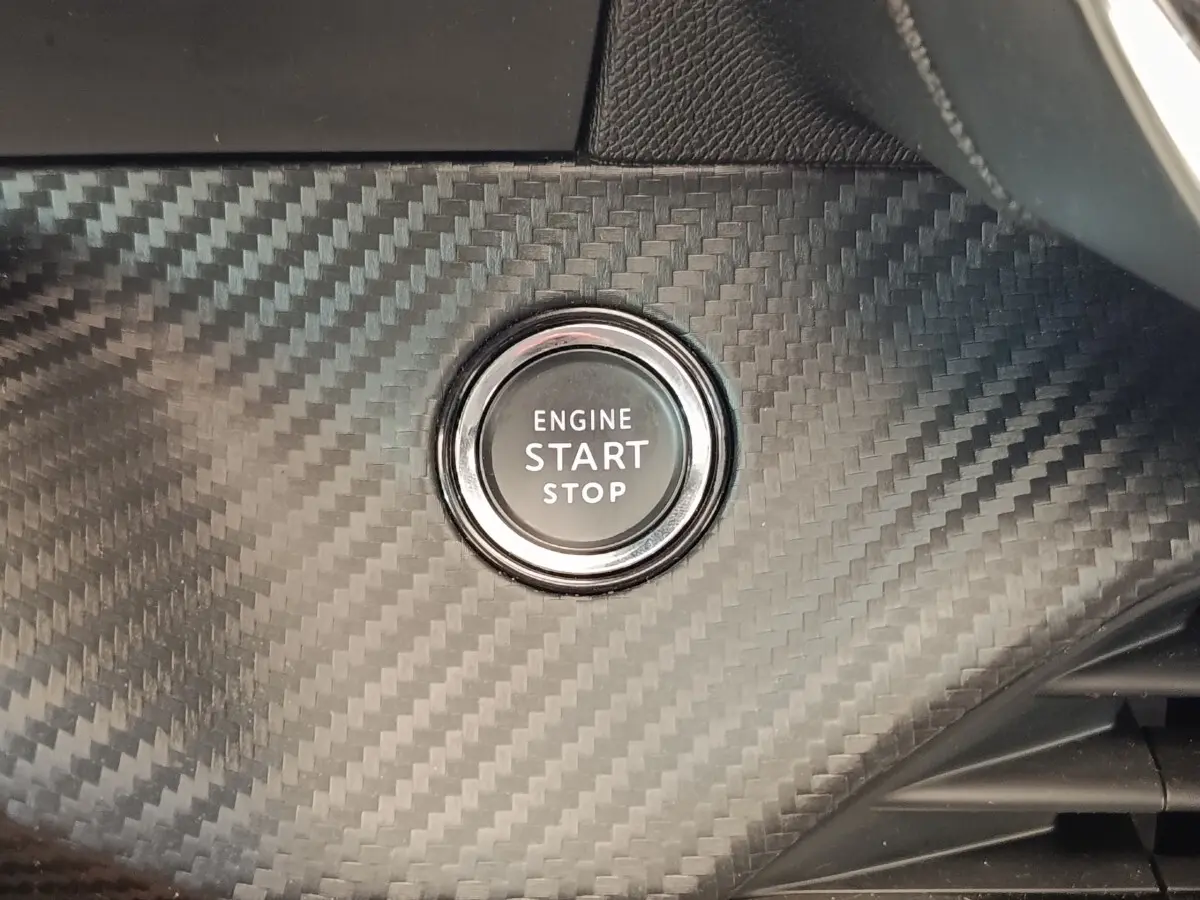 Gros plan sur le bouton start/stop entouré d'un décor noir effet carbone dans l'habitacle d'une Peugeot 208 blanche.