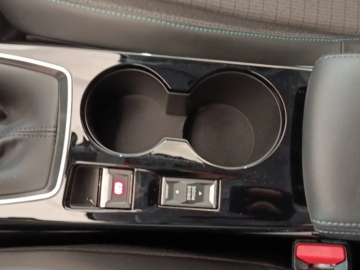 Gros plan sur la console centrale noire du Peugeot 208 blanc, montrant porte-gobelets et commandes mode de conduite et frein électrique.