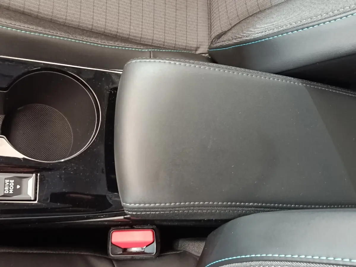 Gros plan sur l'accoudoir central noir et la console avec porte-gobelet de la Peugeot 208 PureTech 100 blanche.