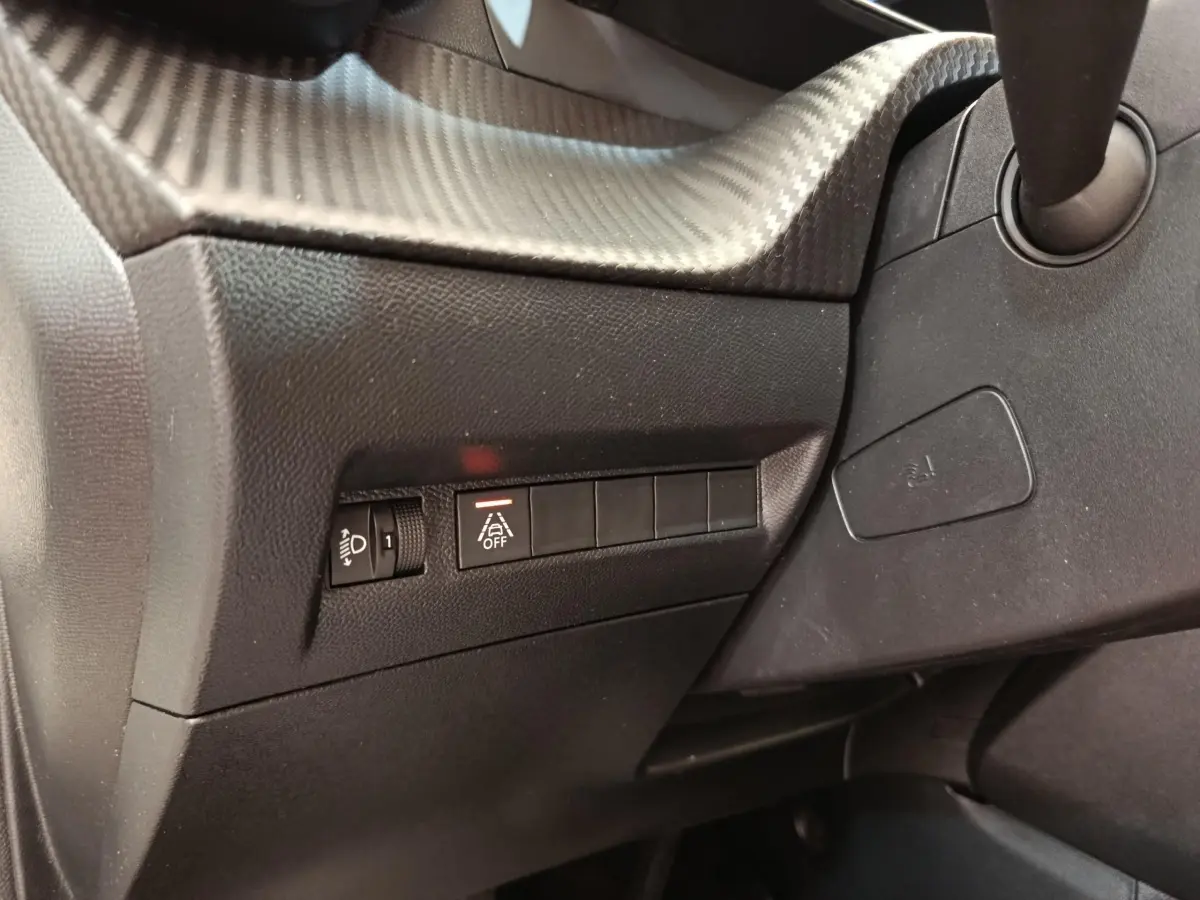 Détail du tableau de bord côté gauche de la Peugeot 208 blanche, avec commandes d'éclairage et d'aide à la conduite.