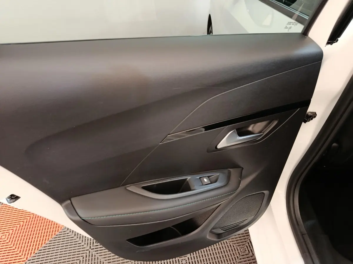 Vue rapprochée de la porte avant droite noire avec poignée argentée et commande de vitre sur Peugeot 208 blanc.