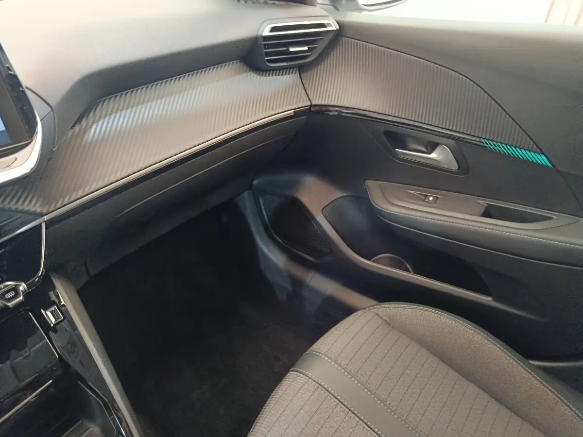 Vue intérieure côté passager de la Peugeot 208 PureTech 100 Allure Business, tableau de bord noir avec insert effet carbone.