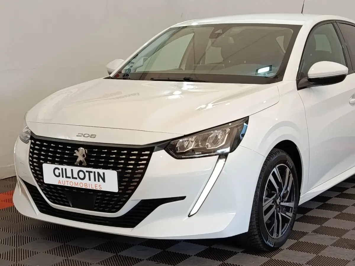 Peugeot 208 blanc vue 3/4 avant droit, avec calandre noire distinctive et feux LED en forme de griffes.