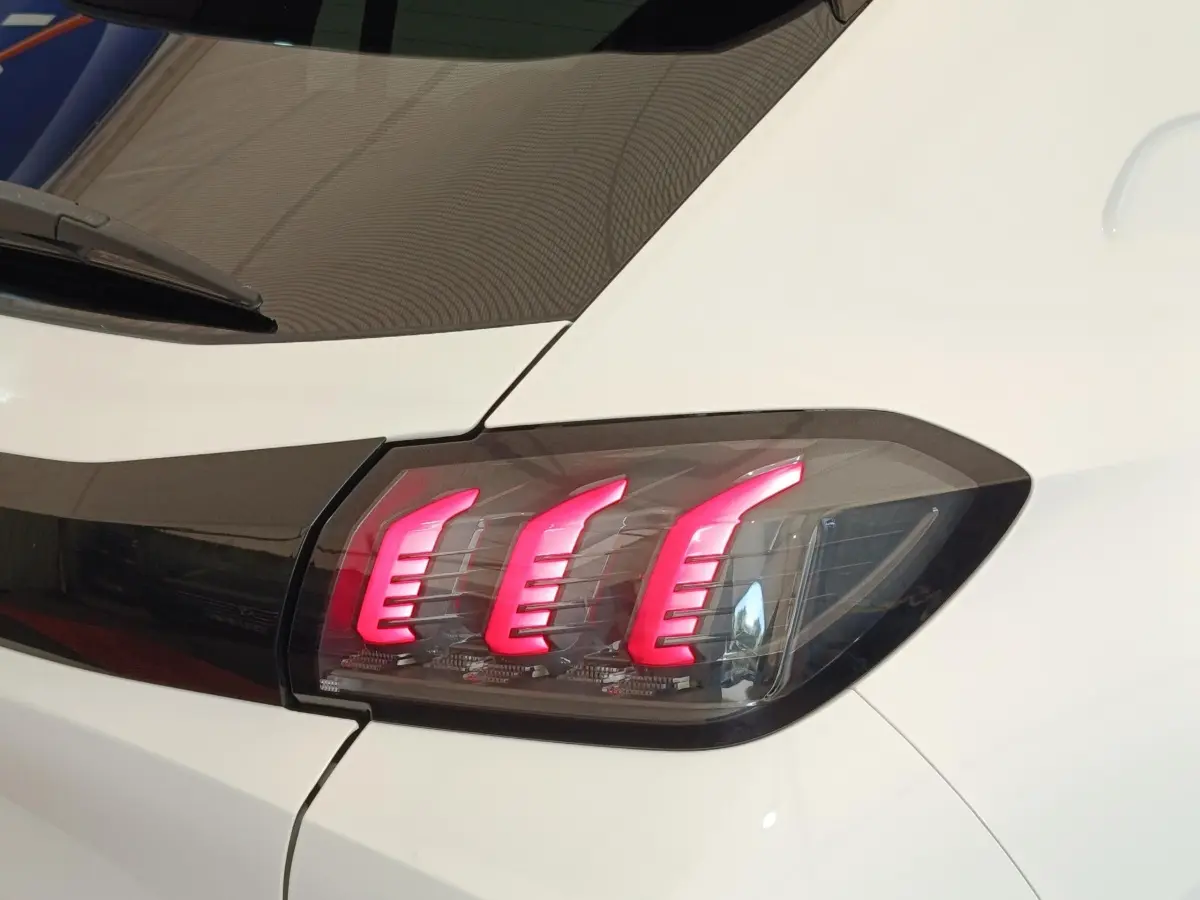 Gros plan sur le feu arrière droit allumé d’une Peugeot 208 blanche, soulignant ses trois griffes lumineuses rouges.
