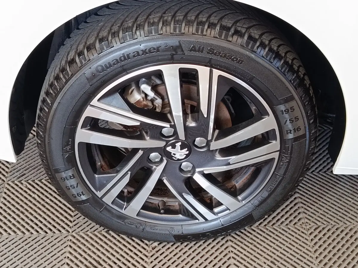 Gros plan sur la roue avant droite d'une Peugeot 208 blanche avec jante alliage noire et argentée.