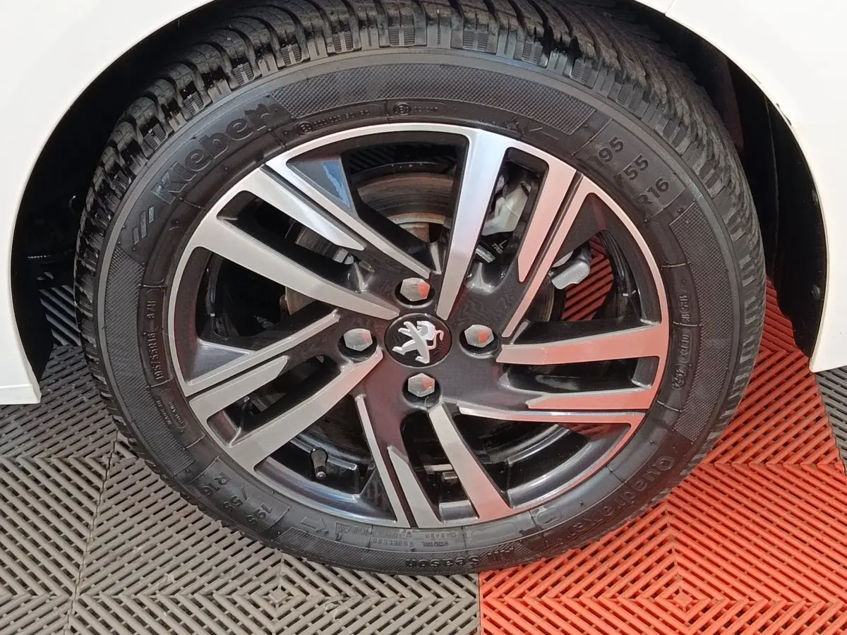 Gros plan sur la jante alliage bicolore avec logo Peugeot, roue avant droite d'une Peugeot 208 blanche.