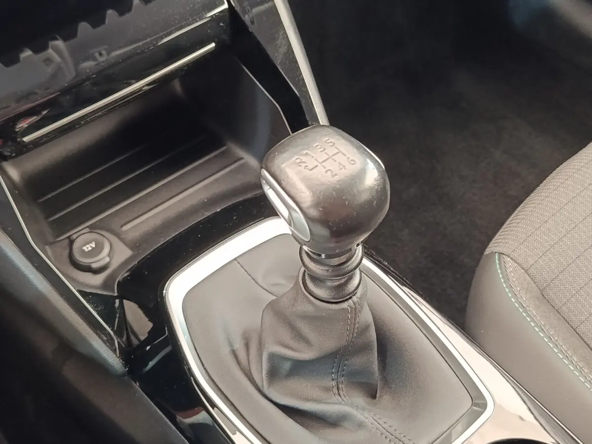 Gros plan sur le levier de vitesses manuel noir et console centrale brillante dans l’habitacle d’une Peugeot 208 blanche.