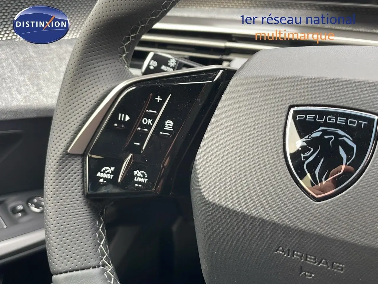 Gros plan sur le volant en cuir perforé du Peugeot 5008 gris, avec commandes intégrées et logo lion central.