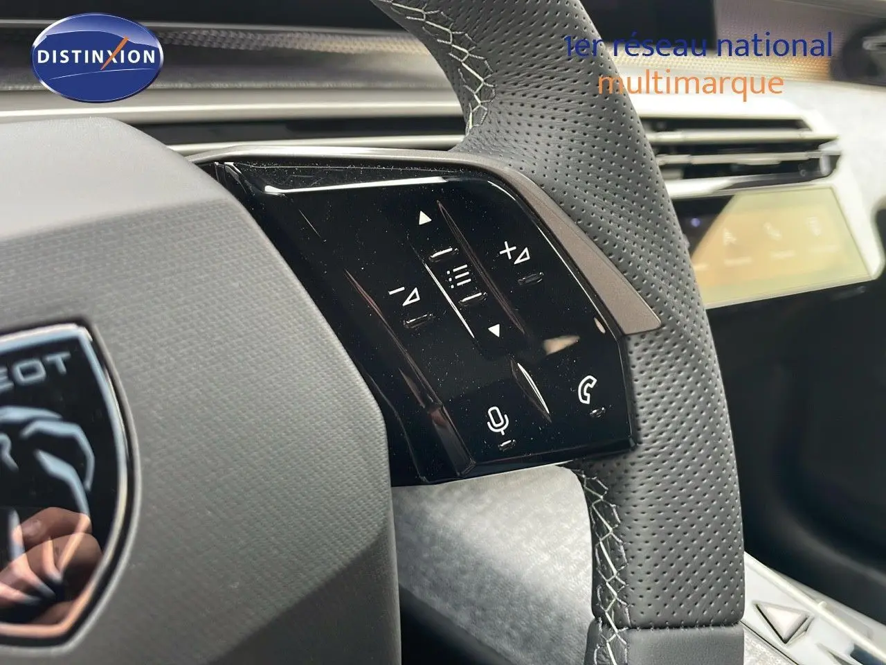 Gros plan sur le volant en cuir perforé gris du Peugeot 5008 Hybrid 2025 avec commandes audio intégrées.
