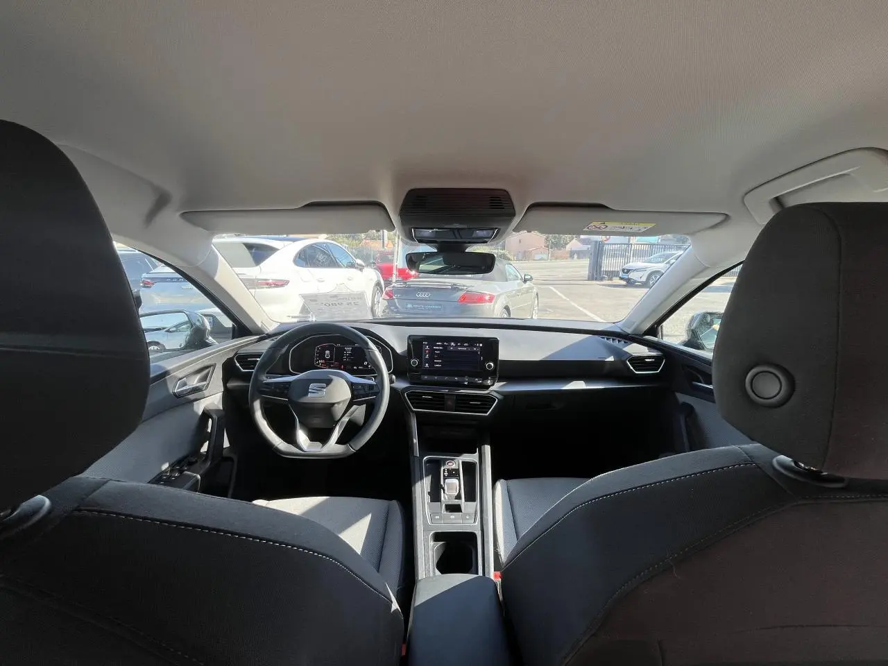 Vue intérieure avant du SEAT Leon IV gris, mettant en valeur le volant cuir multifonction et l'écran digital central.