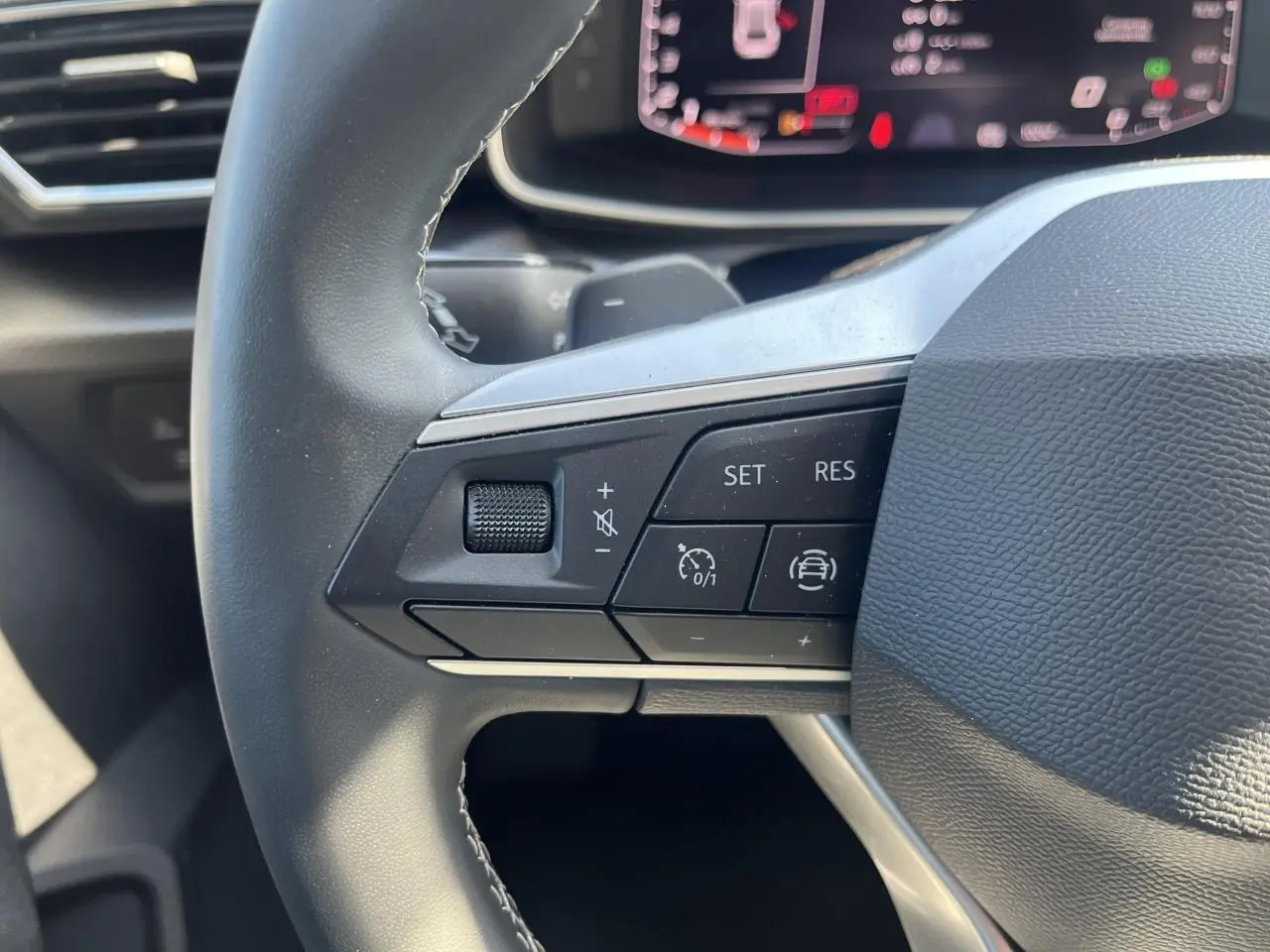 Gros plan sur les commandes du volant cuir multifonction du SEAT Leon IV gris Magnetic Metal, affichage numérique en arrière-plan.