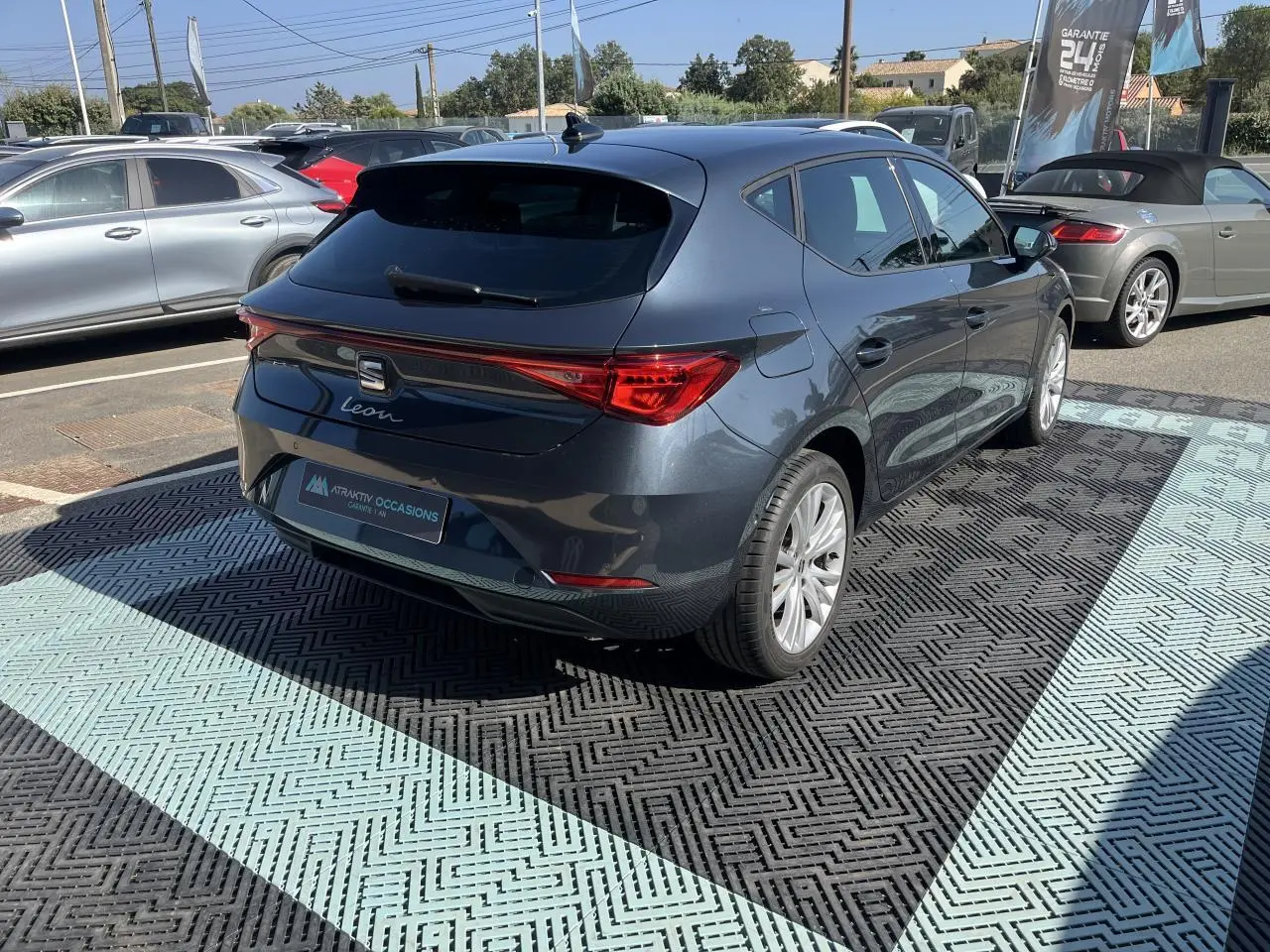 Vue 3/4 arrière droite d'une SEAT Leon IV gris magnetic metal stationnée, soulignant ses feux arrière LED et jantes alliage 17 pouces.