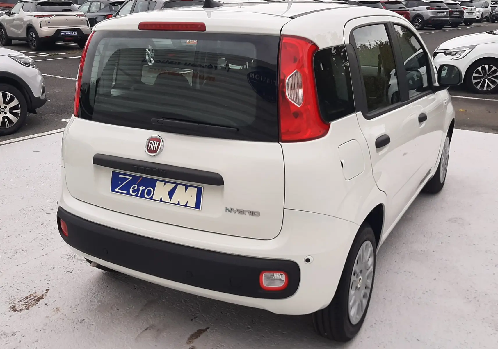 Vue 3/4 arrière droite d'une Fiat Panda blanc gelato avec feux arrière verticaux et hayon noir dans un parking extérieur.