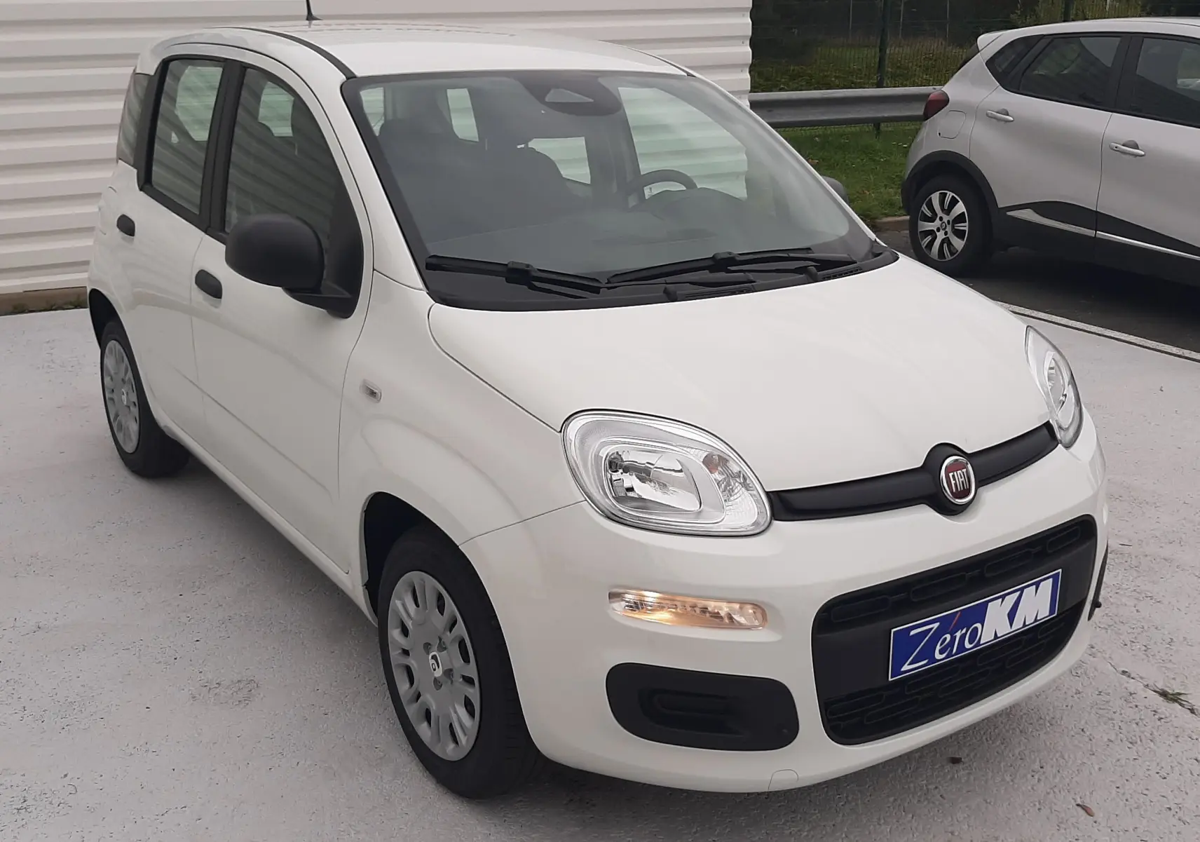 Vue 3/4 avant droite d'une FIAT Panda blanche Gelato avec feux allumés et plaques Zero KM visible.