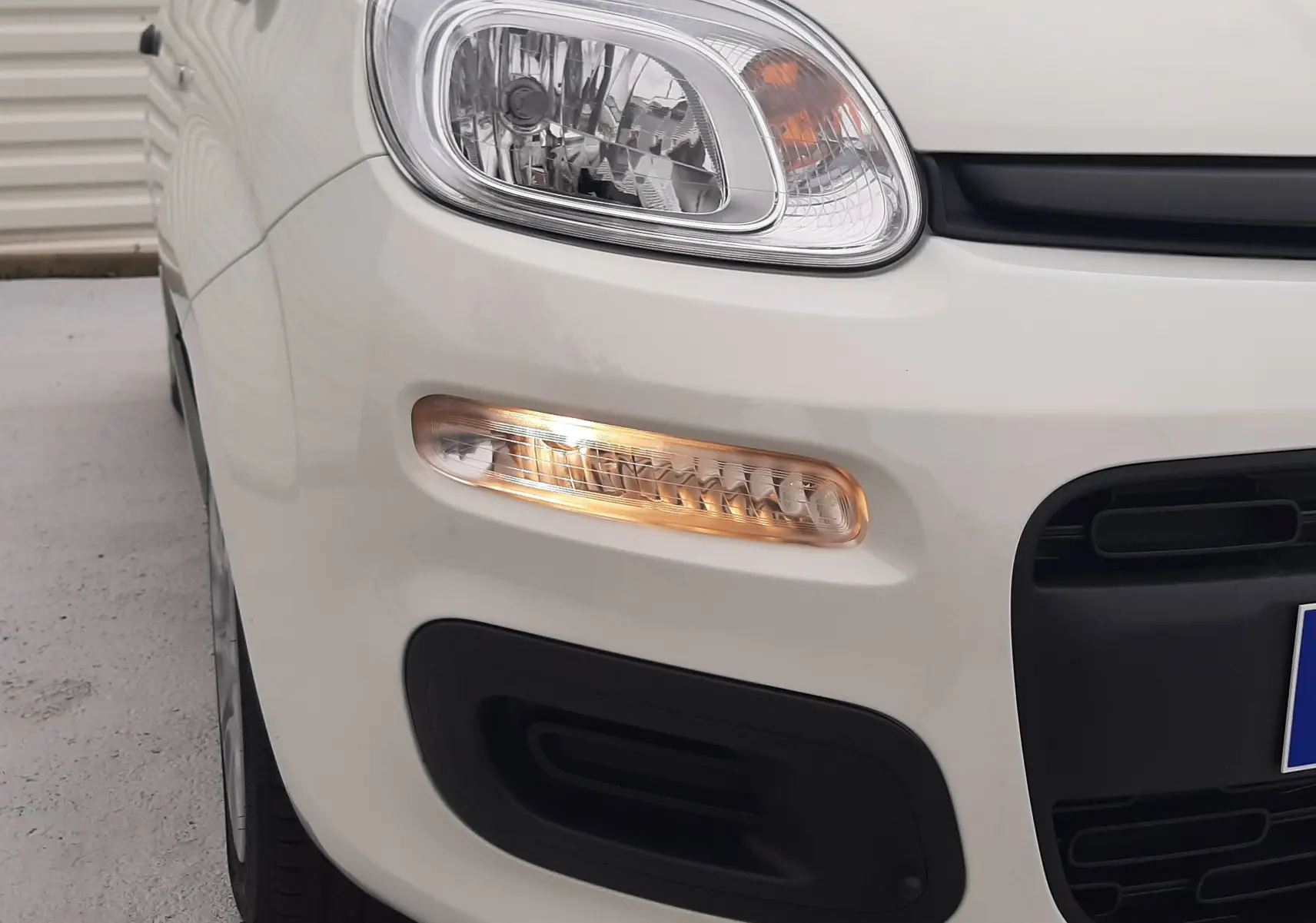 Gros plan sur le phare avant gauche et le clignotant allumé d'une Fiat Panda 2025 blanc gelato, avec pare-chocs noir.