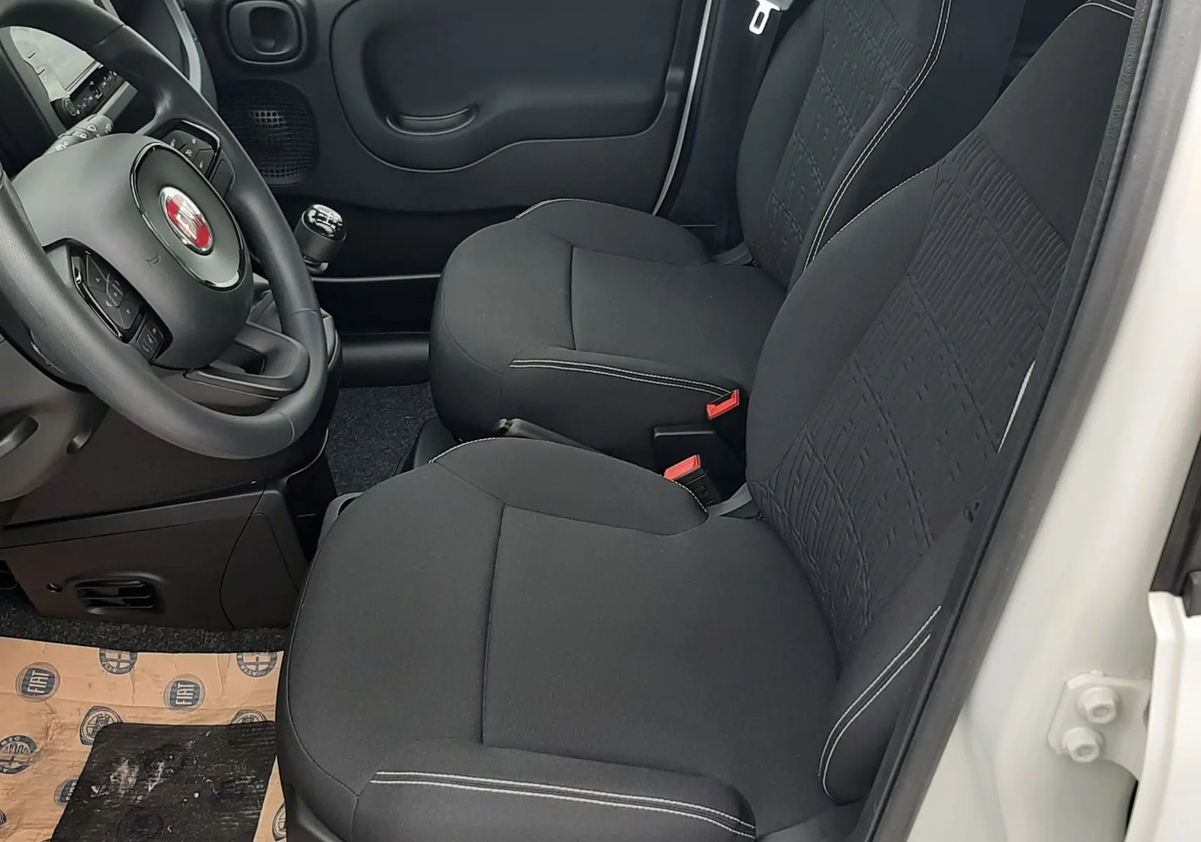 Vue intérieure côté conducteur de la Fiat Panda blanc gelato 2025, sièges noirs en tissu et volant multifonction.