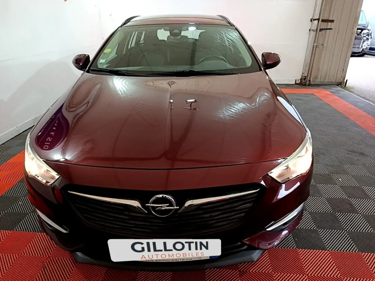 Vue avant d'une Opel Insignia rouge 2019 avec phares allumés et calandre chromée dans un garage.