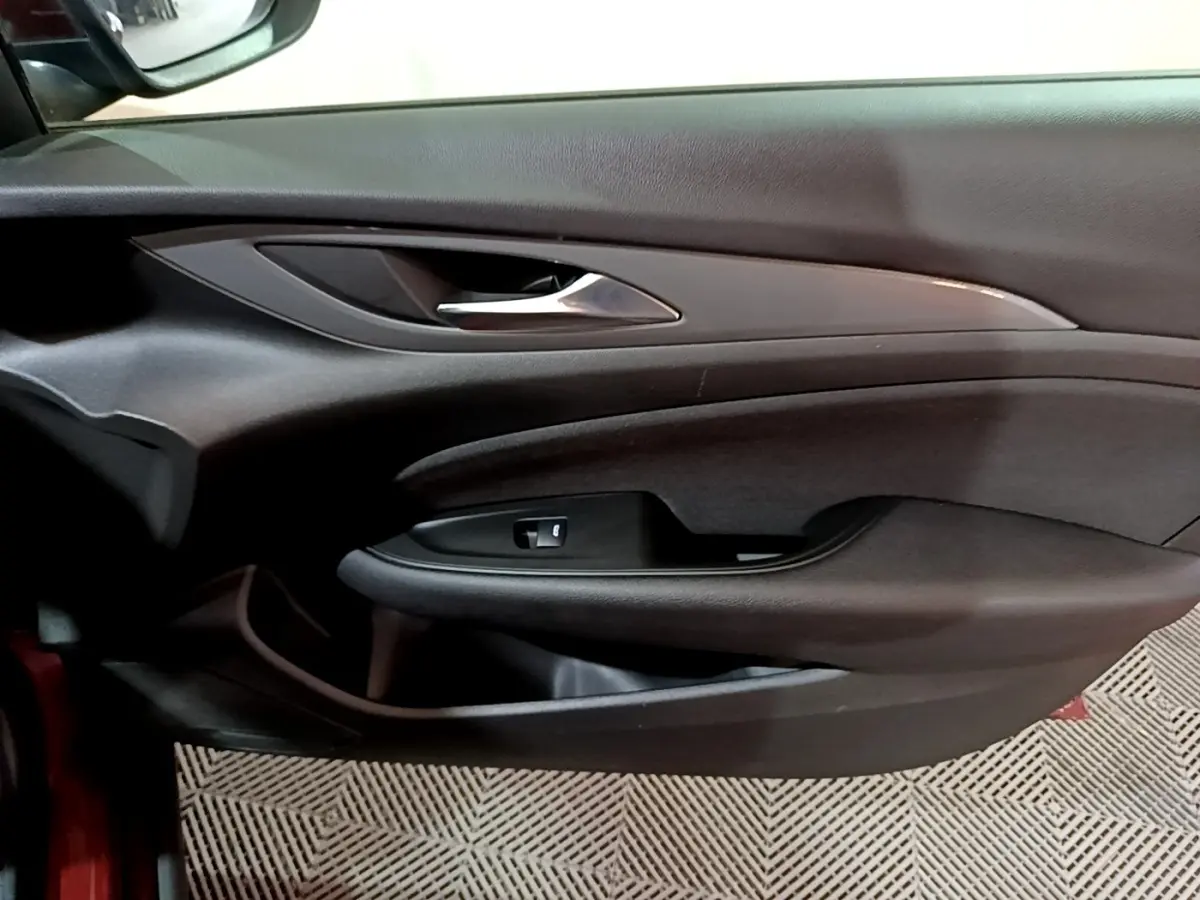 Vue rapprochée de la porte intérieure côté gauche de l’Opel Insignia rouge, avec poignée chromée et commande de vitre.