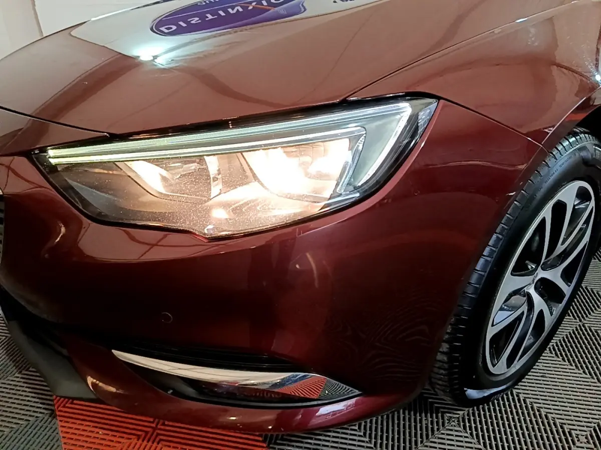 Gros plan sur le phare avant gauche et la roue d’une Opel Insignia rouge métallisée, finition Edition Business.