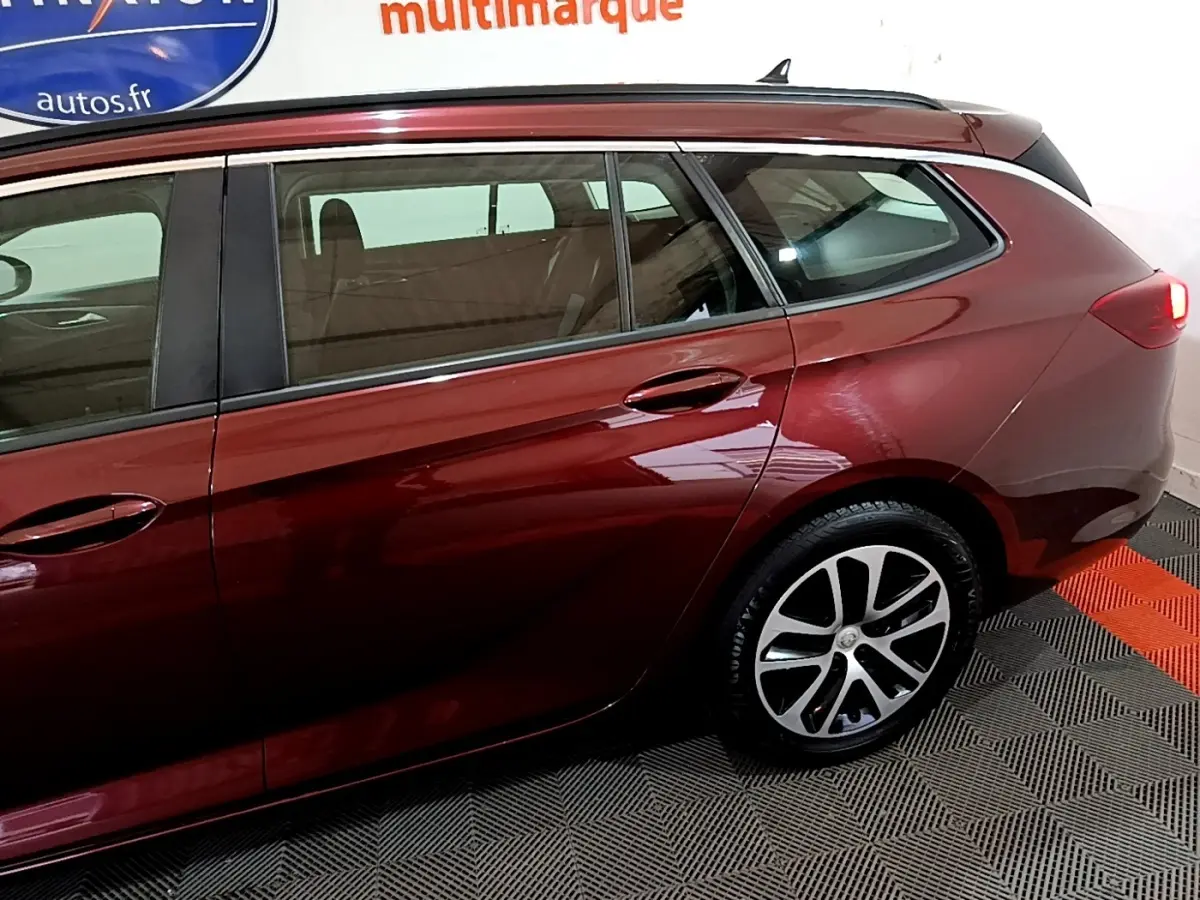Vue latérale côté droit d'une Opel Insignia break rouge métallisé, mettant en valeur la roue arrière et les vitres teintées.