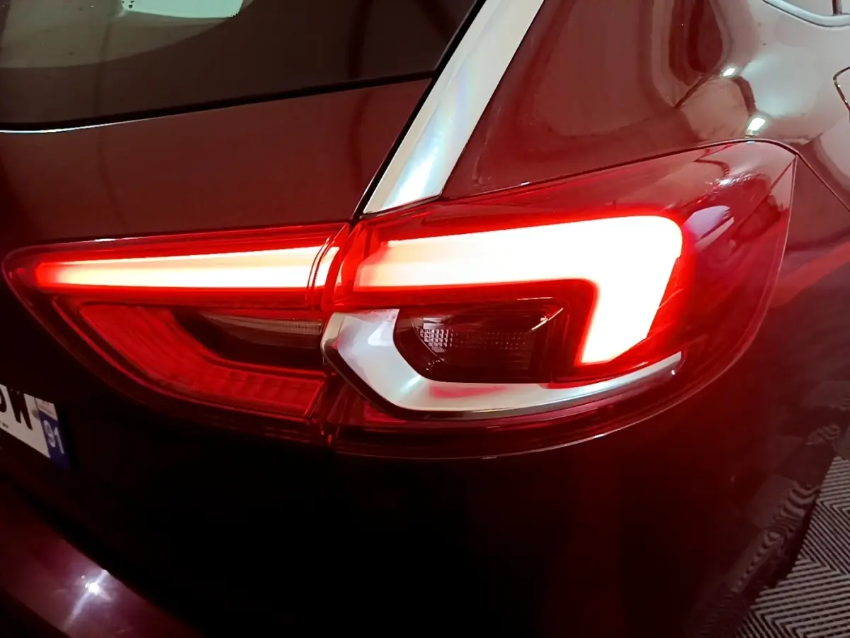 Gros plan sur le feu arrière droit rouge allumé d’une Opel Insignia rouge, vue arrière en faible luminosité.