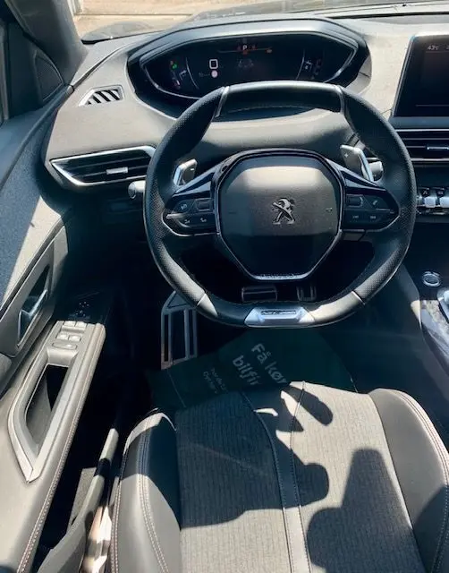 Vue intérieure centrée sur le volant compact du Peugeot 3008 noir 2018, avec tableau de bord numérique et commandes intégrées.