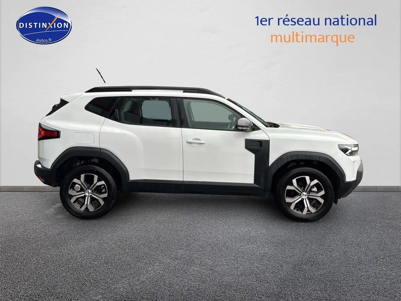 Profil côté gauche du Dacia Duster blanc arctic 2025 avec jantes alu et barres de toit noires.