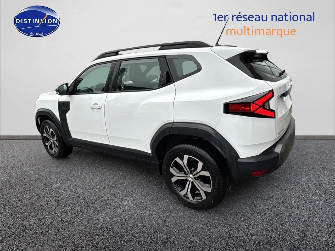 Vue 3/4 arrière droite du Dacia Duster blanc Arctic avec barres de toit et jantes alliage noires.