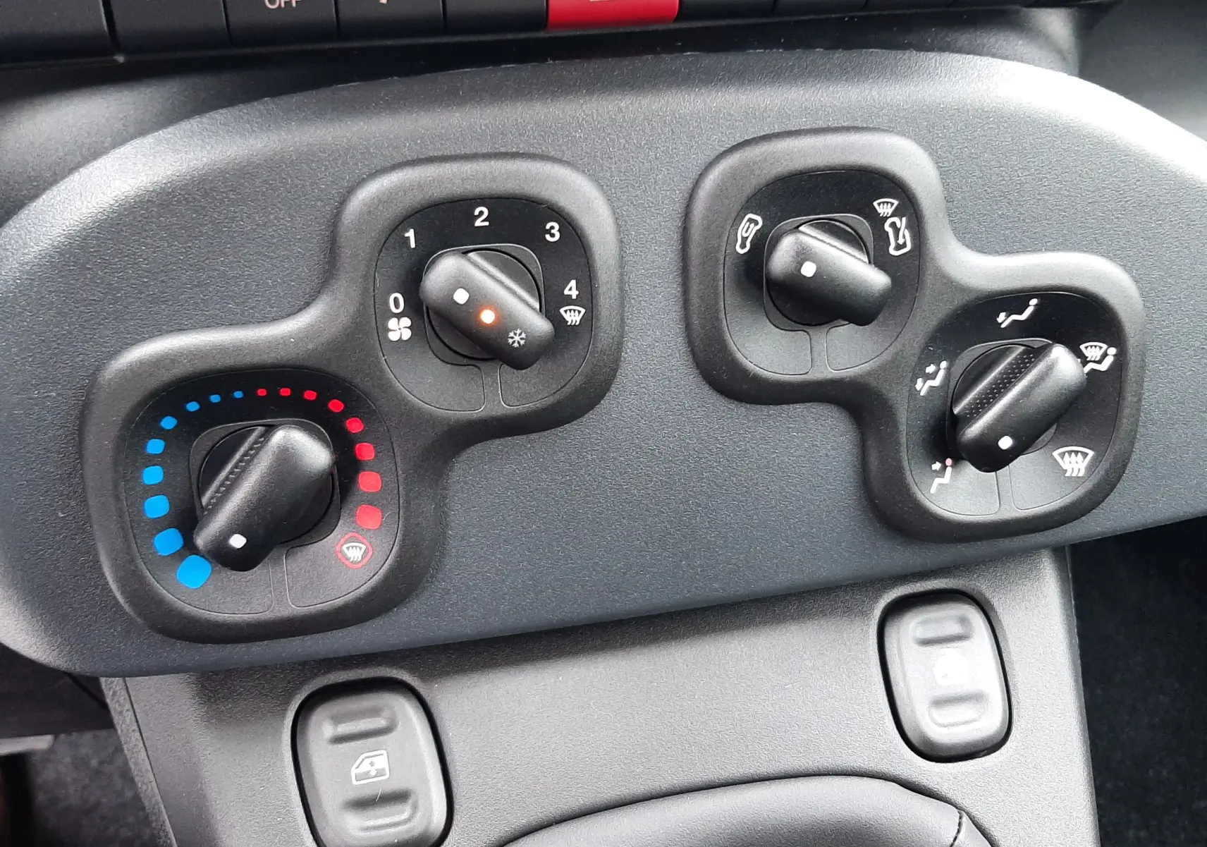 Commandes de climatisation et boutons de sécurité sur tableau de bord noir de la Fiat Panda 2025.