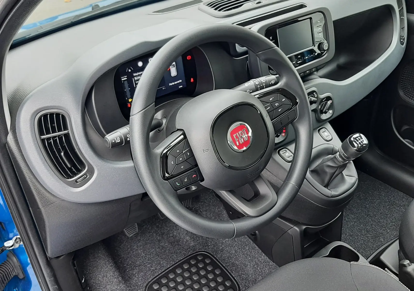 Vue intérieure côté conducteur de la Fiat Panda 2025 bleu Italia, volant multifonction et levier de vitesse manuel visibles.