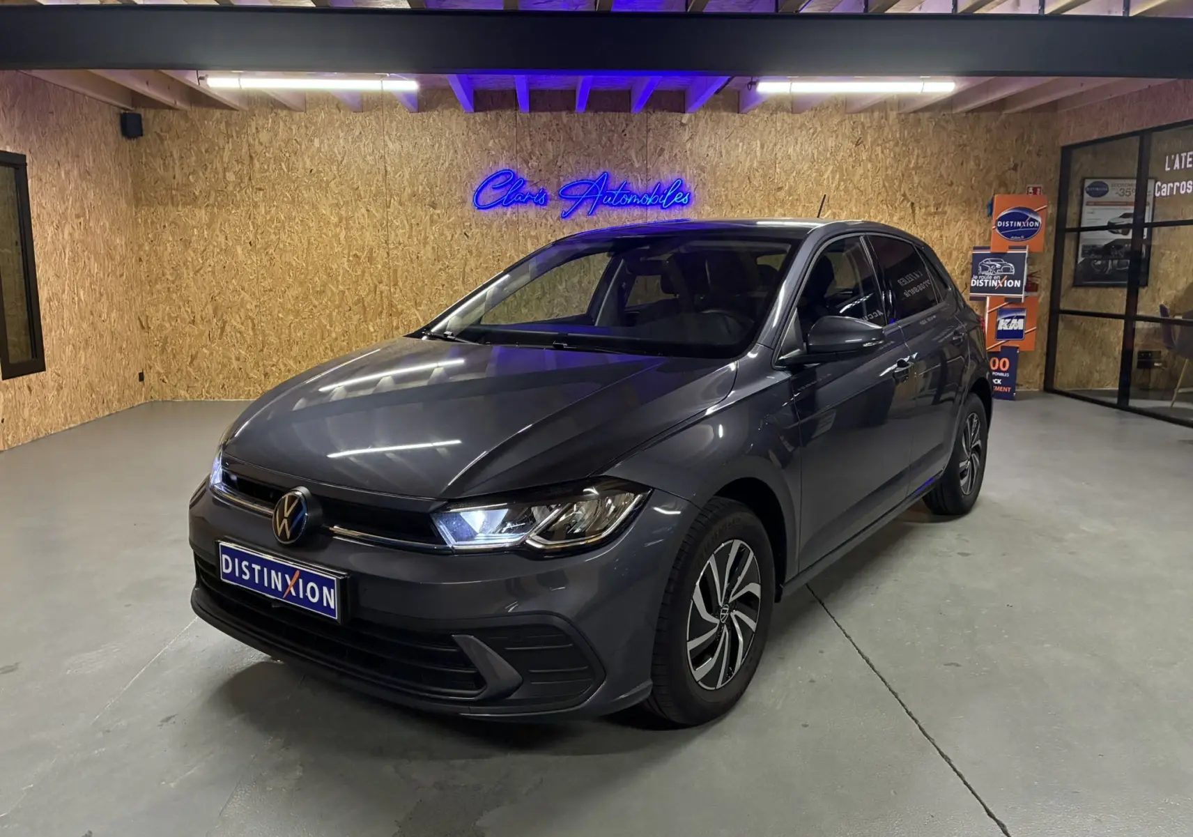 Volkswagen Polo gris en 3/4 avant droit dans un showroom avec éclairage bleu et jantes bi-ton.