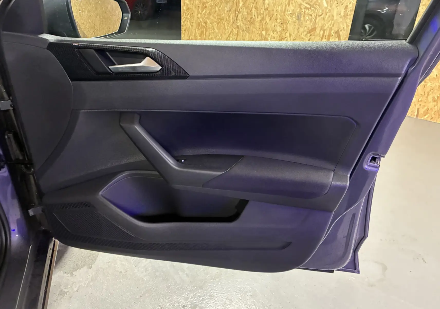 Vue intérieure de la porte côté gauche d'une Volkswagen Polo gris 2025, avec poignée argentée et garniture noire.