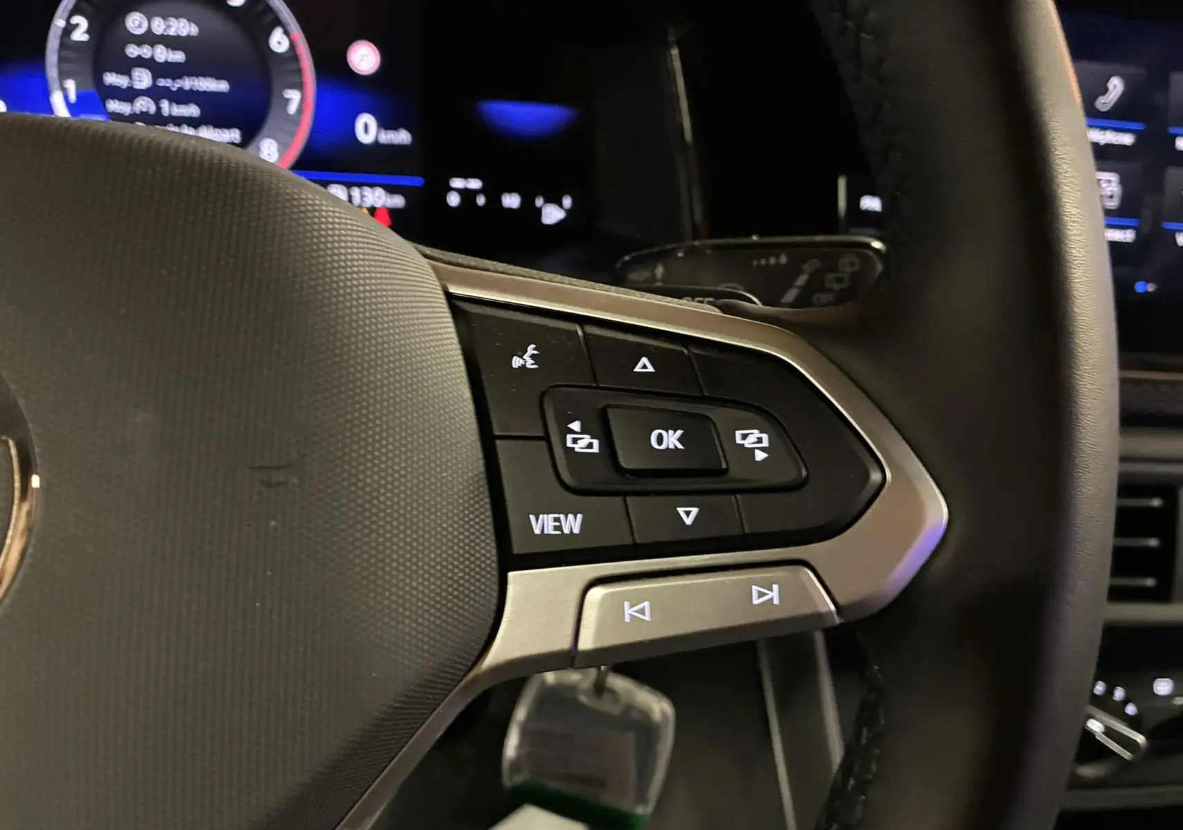 Gros plan sur les commandes multifonctions à droite du volant noir de la Volkswagen Polo VI gris, avec affichage numérique en arrière-plan.