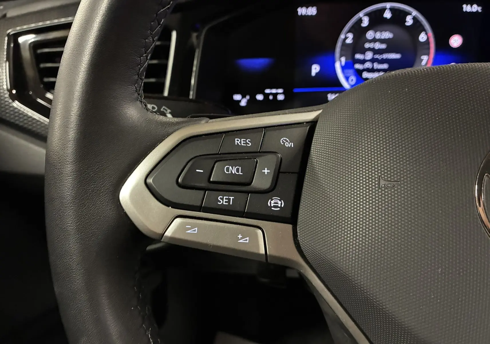 Gros plan sur les commandes au volant à gauche d'une Volkswagen Polo gris 2025, avec tableau de bord numérique en arrière-plan.