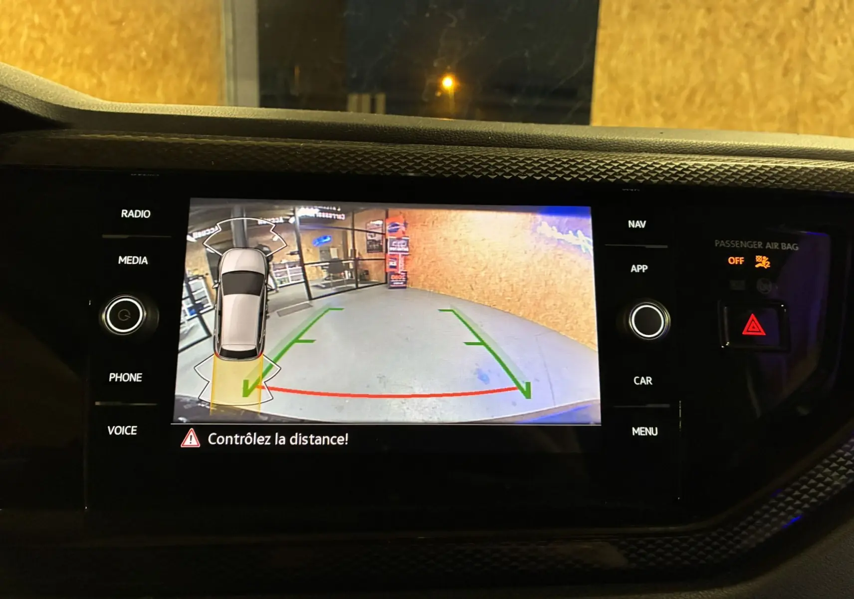 Vue de l'écran de recul du tableau de bord d'une Volkswagen Polo grise, avec guidage de trajectoire et alertes visibles.