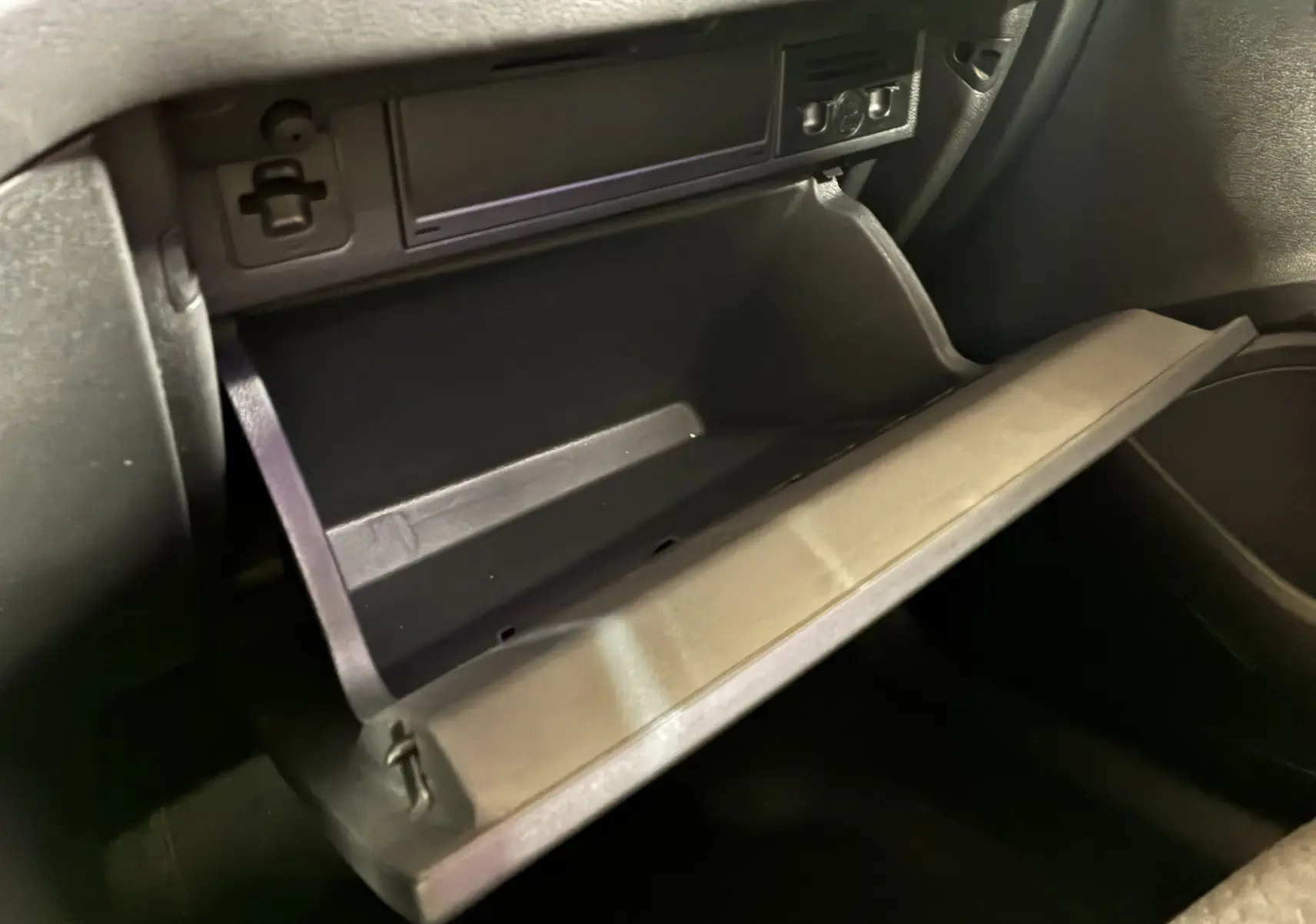 Gros plan sur la boîte à gants ouverte de la Volkswagen Polo gris, montrant l'intérieur en plastique noir.