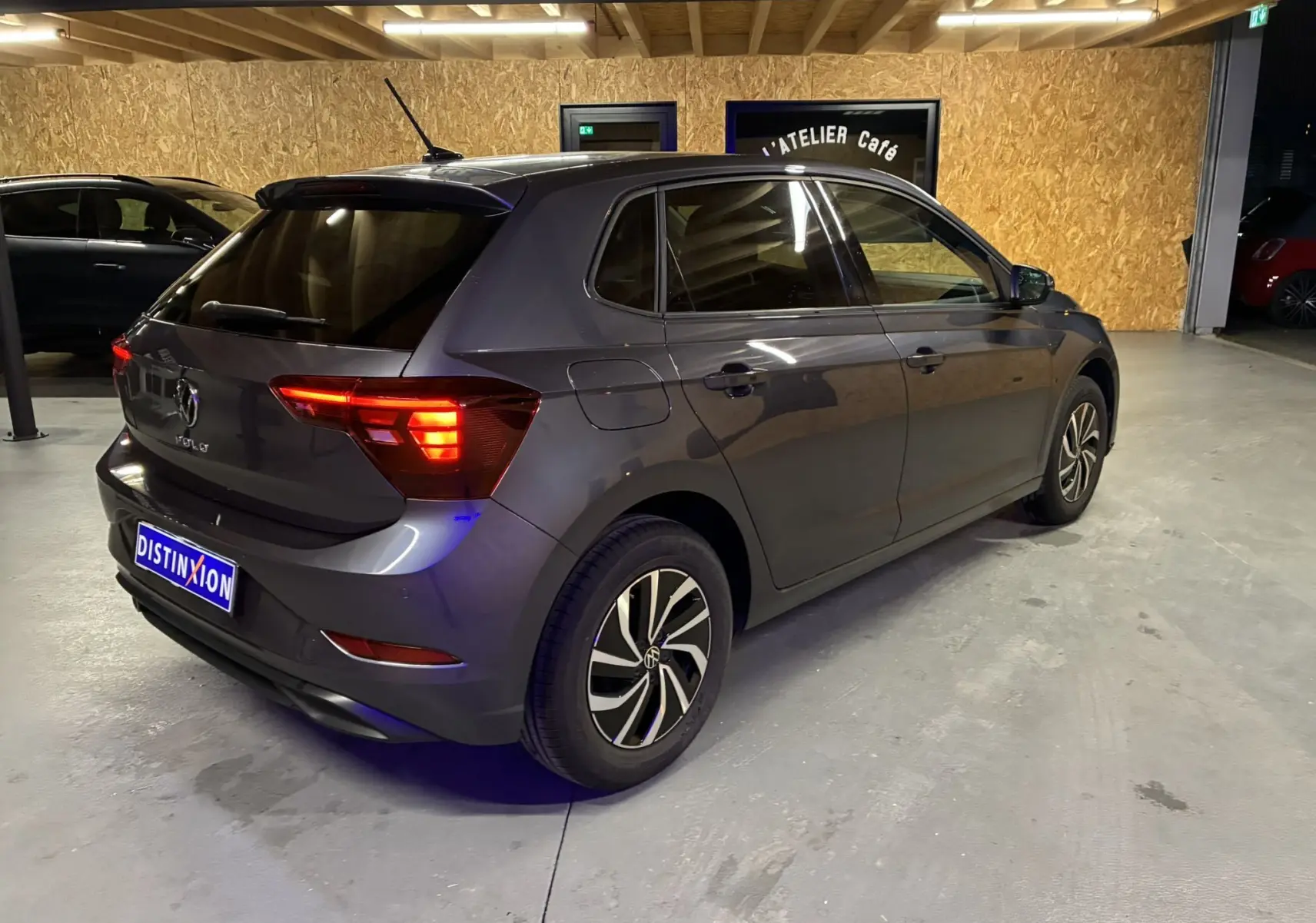 Volkswagen Polo gris vue 3/4 arrière droit en intérieur avec feux arrière allumés et jantes bi-ton.
