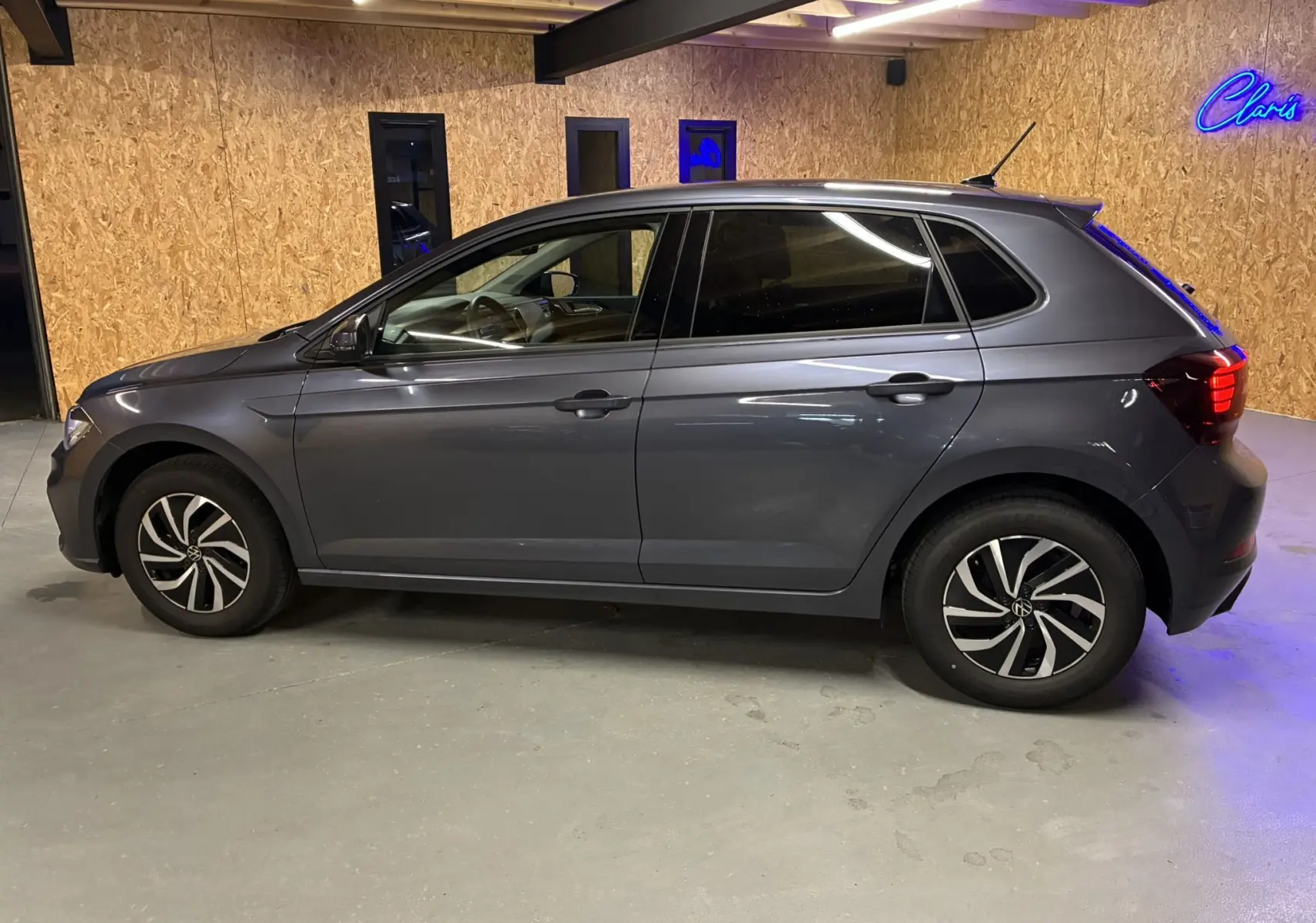 Profil côté gauche d'une Volkswagen Polo gris métallisé 2025 avec jantes bi-ton et cinq portes dans un garage.